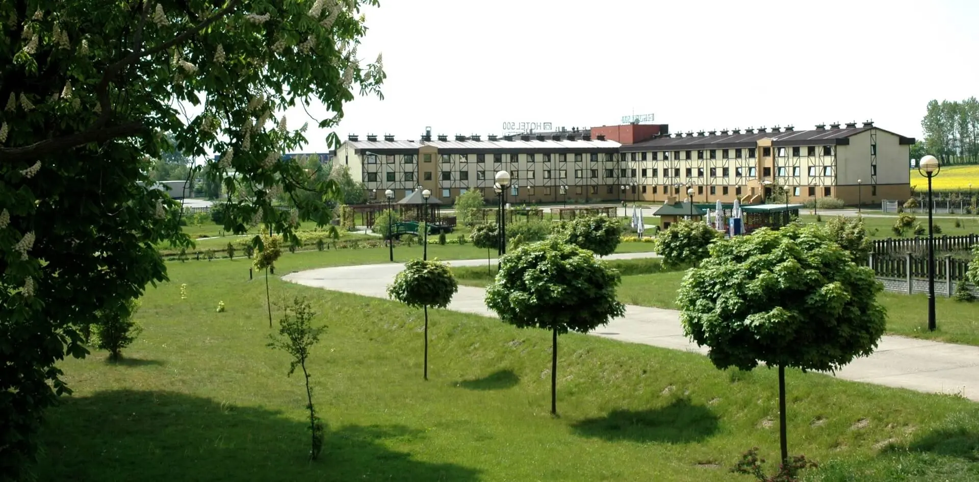 Hotel 500 Tarnowo Podgórne otoczony zielenią, z ogrodem i alejkami na terenie obiektu.